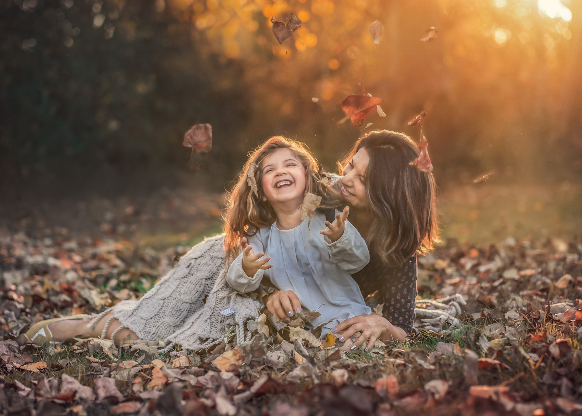 Madre e hija riendo entre hojas de otoño